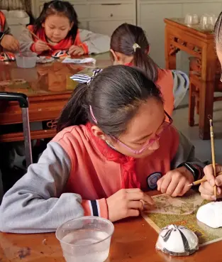  ??  ?? Yang Yudong, a successor of the intangible cultural heritage colorful Peking Opera masks, is teaching pupils how to paint Peking Opera facial masks.