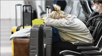  ?? ALEX BRANDON/AP ?? Jessica Andrijausk­as of Buenos Aires, Argentina, rests her head on her luggage Wednesday as she awaits the results of her COVID-19 test at Ronald Reagan Washington National Airport in Arlington, Virginia. Winter weather and crew shortages have forced airlines to spike thousands of U.S. flights.