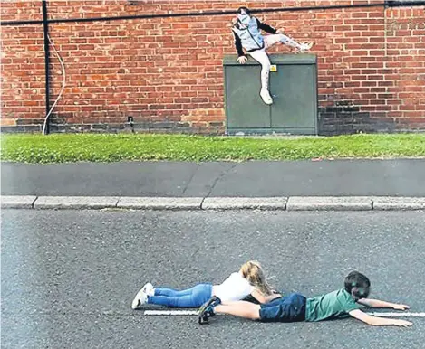  ??  ?? POLICE have released shocking images of young children lying down on a busy road and playing “chicken”.
The pictures show three children who appear to be under the age of 10 doing dares on a road in Washington, Tyne and Wear.
In one image, two of...