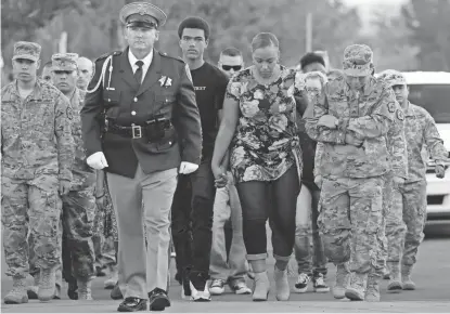  ?? AP PHOTOS ?? Veronica Hartfield, center right, walks alongside her son, Ayzayah Hartfield, center, as they arrive at a candleligh­t vigil for her husband, Las Vegas Police Officer Charleston Hartfield, on Thursday.