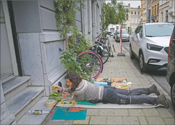  ??  ?? Lemmens lays on the sidewalk as she installs a miniature scene into a boot-scraper.