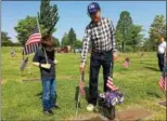  ?? CHAD FELTON — THE NEWS-HERALD ?? Palmer-Roberts American Legion Post 214 member John Perry places a new flag at Western Reserve Memorial Gardens May 24 while his 6-year-old grandson, Wyatt, looks to follow suit.