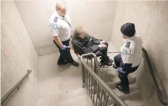  ??  ?? Ellen Tremblay, 70, is carried up a stairwell to the fifth floor of the Ashlar Manor by MediVan workers. The elevator has been repaired after being shut down for nearly two weeks.