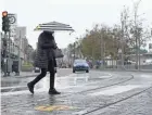  ?? JEFF CHIU/AP ?? A pedestrian carries an umbrella while crossing a street at Fisherman's Wharf in San Francisco as showers drifted across the drought-stricken and fire-scarred landscape of Northern California.