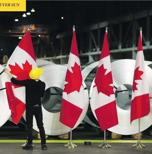  ?? PETER POWER / THE CANADIAN PRESS ?? A worker at Stelco in Hamilton, Ont., straighten­s Canadian flags in front of rolls of coated steel before a visit by Foreign Affairs Minister Chrystia Freeland Friday. Freeland met with employees at the plant and announced the government’s latest response to U.S. tariffs on steel and aluminum.