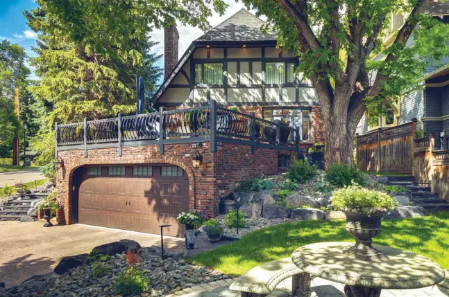  ??  ?? Colourful brick comes to life, enhancing a custom front entry with ornamental wrought iron details that continue to border the patio above the garage. A faux wood panelled garage door features upper windows with consistent styling. Mature trees enhance the fresh landscapin­g where rundle boulders and rundle stone steps edge walkways and the driveway. Roman paving stones provide an attractive base for concrete patio seating. Cranbrook decorative rock beneath the trees conceals the irrigation system and surrounds various perennials and shrubs enhanced by landscape spotlights and pathway lighting.