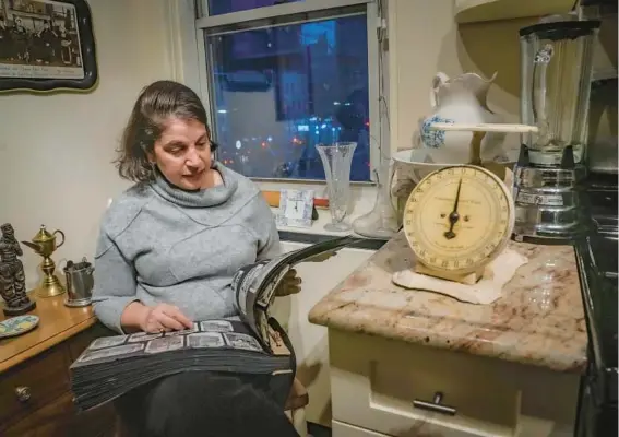  ?? BEBETO MATTHEWS/AP ?? Anne D’Innocenzio flips through a family album Feb. 26 in her kitchen, surrounded by mementos from her childhood home in New Jersey, at her New York residence.
