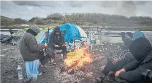  ?? KIRAN RIDLEY GETTY IMAGES ?? Refugees sit by a fire in Dunkirk, France, on Thursday. At least 27 migrants died in a bid to cross the English Channel on Wednesday. Officials have vowed to crack down on channel crossings.