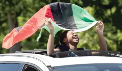  ?? PAT NABONG/SUN-TIMES FILES ?? A paradegoer laughs while holding a flag during last year’s West Garfield Park Juneteenth Parade.