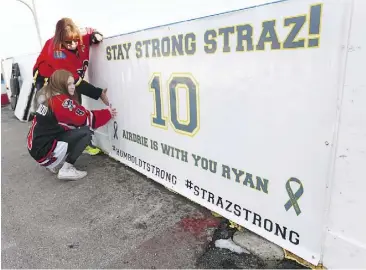  ?? JIM WELLS ?? Tracey Shea, standing, and Taya Nelson ready a sign along the boards in Airdrie during a vigil for local hockey player Ryan Straschnit­zki, who was paralyzed in the Humboldt crash.