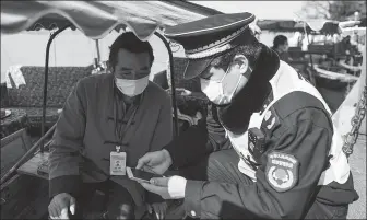  ?? WANG GANG / CHINA NEWS SERVICE ?? A boatman (left) who works at the West Lake Scenic Area has his health code, which is shown on his smartphone, checked. The attraction in Hangzhou, Zhejiang province, has partially resumed its boat services.