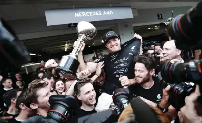  ?? — AFP ?? SUZUKA: Japanese Grand Prix winner Mercedes AMG Petronas F1 Team’s German driver Nico Rosberg holds his trophy as Mercedes AMG Petronas members celebrate at their paddock after the Formula One Japanese Grand Prix race in Suzuka yesterday.