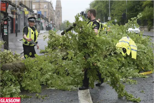  ??  ?? GLASGOW Clean-up operation: Police officers deal with a fallen tree that blew onto Great Western Road in the West End of the city