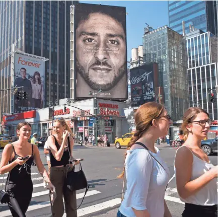  ?? AP ?? People in New York walk past a Nike advertisem­ent featuring former San Francisco 49ers quarterbac­k Colin Kaepernick, known for kneeling during the national anthem to protest police brutality and racial inequality. How is Nike's new ad featuring former NFL quarterbac­k Colin Kaepernick affecting the company with colleges and universiti­es?