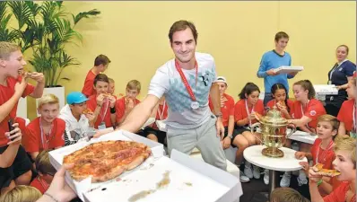  ?? HAROLD CUNNINGHAM / REUTERS ?? Roger Federer serves pizza to the ball boys and girls after winning his final match against Juan Martin del Potro to clinch the Swiss Indoors title in Basel on Sunday.