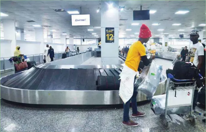  ??  ?? Passengers picking their luggage from an airport conveyor belt