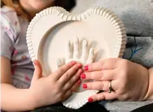  ?? ?? Jessica Day-Weaver right, and Caitlin Weaver hold up a ceramic hand print of daughter, Anastasia, at their home, Thursday, Feb. 2, 2022, in Boardman, Ohio.(AP Photo/Nick Cammett)