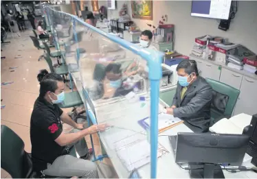  ?? APICHART JINAKUL ?? RIGHT
People filing official documents speak to officials through a small window in a transparen­t screen at the Watthana district office. The screen was put up to prevent the spread of Covid-19.