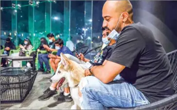  ?? AFP ?? Mask-clad patrons sit with their dogs at the ‘Barking Lot’ cafe in Saudi Arabia’s eastern Gulf city of Khobar.