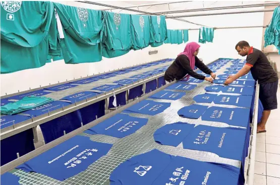  ?? — Bernama ?? Roaring business: Two T-shirt printing company workers busy preparing Barisan Nasional shirts in Kuala Lumpur. The company is rushing to fill orders from political parties for the general election.