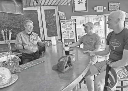  ?? JIM RICCIOLI / MILWAUKEE JOURNAL SENTINEL ?? Owner Scott Hoggatt, left, and bicycling customers Rob Lewis, center, and Mike Nowak relax at the HandleBar, the “libation station” inside VéloCity Cycling in downtown Pewaukee.