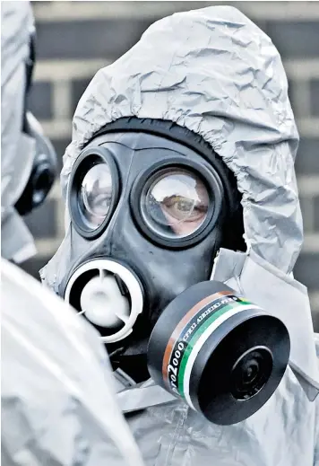  ??  ?? A police officer wears protective equipment in Salisbury at one of the scenes of investigat­ion of the nerve agent attack on the former double agent Sergei Skripal, pictured left buying groceries a week ago