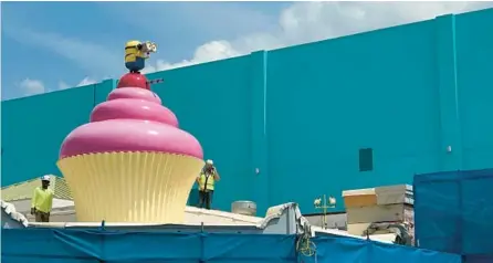  ?? DEWAYNE BEVIL/ORLANDO SENTINEL ?? Workers at Universal Studios theme park stand on the roof next to a cupcake, topped by a Minion character.