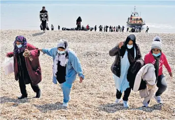  ??  ?? Migrants make their way up the beach after arriving on a small boat at Dungeness in Kent earlier this month