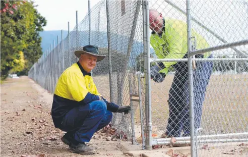  ?? Picture: STEWART McLEAN ?? ESCAPE ROUTE: Cairns Regional Council workers Luke Boniface and James Dunne install a one-way gate in the fence at Trinity Beach Sports Precinct AFL grounds so wallabies can get out.