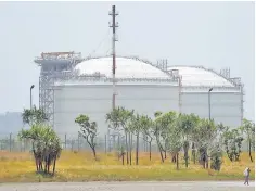  ??  ?? A woman carrying a bag containing firewood walks in front of two Liquefied Natural Gas (LNG) storage tanks at the ExxonMobil PNG Ltd operated LNG plant at Caution Bay, on the outskirts of Port Moresby, Papua New Guinea. France’s Total and partners on Tuesday signed a long-awaited deal to develop gas fields to feed two new production units at the plant. — Reuters photo