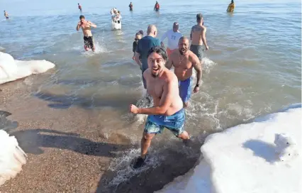  ?? PHOTOS BY MIKE DE SISTI/MILWAUKEE JOURNAL SENTINEL ?? Rolando Gonzalez and his father, Rolando Gonzalez (behind), run out of the water after their chilly dip as hundreds of brave souls took park in Milwaukee’s annual Polar Bear Plunge at Bradford Beach on Lake Michigan. See more photos and a video at...