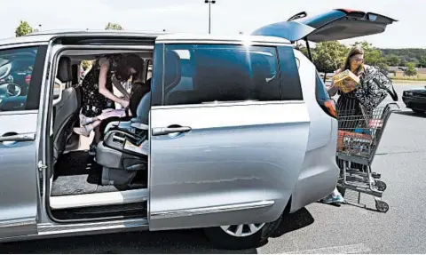  ?? JESSICA HILL/AP ?? Melanie Matcheson puts groceries into her Chrysler Pacifica as her daughter Georgianna buckles her sister Caroline into a car seat in Southingto­n, Conn.