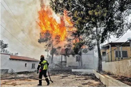  ??  ?? Ein Feuerwehrm­ann kämpft gegen die Flammen in Kineta. Viele Menschen flüchteten mit ihren Autos. Es kam zu Staus.