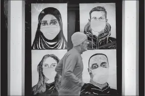  ?? ROBERT F. BUKATY/AP PHOTO ?? A runner passes by a window displaying portraits of people wearing face coverings to help prevent the spread of the coronaviru­s in Lewiston, Maine.