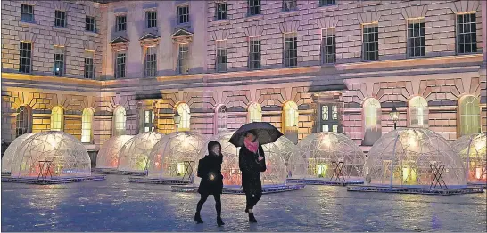  ?? REUTERS ?? People walk past outdoor dining pods, named ‘winter domes’, erected in the courtyard of Somerset House to enable restaurant eating, as England recently lifted some of the pandemic-related curbs .