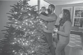  ?? PAULA BRONSTEIN/AP ?? Ani Sirois places lights and decoration­s on the family’s Christmas tree with her 2-year-old daughter Ida and husband, Chadwick, at their home in Portland, Ore., on Tuesday. The family went tree-shopping nearly a week before Thanksgivi­ng.