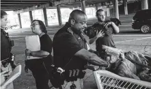  ??  ?? Hensley, who said he did two tours in Iraq, holds his dog, Princess, as Deputy Greg Temple and others hand out Narcan.