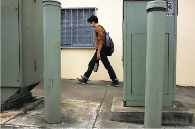  ?? Leah Millis / The Chronicle ?? Resident Brian Dentino walks past utility boxes that AT&T has put up in S.F.’s Outer Sunset District. AT&T is pushing the city to back off on a law requiring the company to paint murals or plant trees to obscure the boxes.