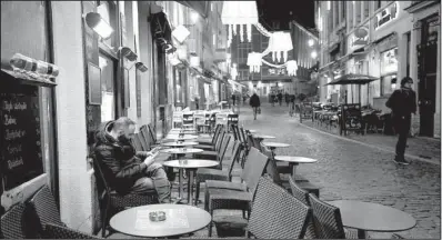  ?? AP/ALASTAIR GRANT ?? A man smokes and looks at his smartphone Monday under a heating lamp in what would normally be a busy tourist area of central
Brussels.