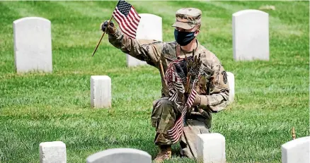  ?? AP ?? A masked soldier places flags at Arlington Cemetery, while audience members, left, wait for President Donald Trump’s address at Fort McHenry on Memorial Day.