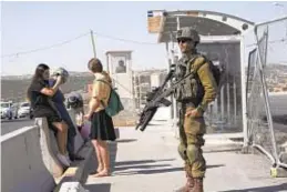  ?? AP ?? An Israeli soldier secures a bus stop while Israeli settlers wait for a ride at a transporta­tion hub for West Bank Jewish settlement­s.