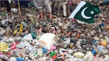  ??  ?? Ayaz Memon Motiwala, 42, an independen­t Pakistani candidate contesting a seat in the National Assembly and two seats for the provincial Sindh Assembly, holds a Pakistan national flag as he lies partially submerged in garbage at a dump during an...