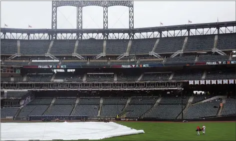  ?? SETH WENIG — THE ASSOCIATED PRESS ?? Members of the Phillies staff retrieve some gear during a rain delay before a game between the Mets and the Phillies at Citi Field on Thursday. The game was postponed due to rain.