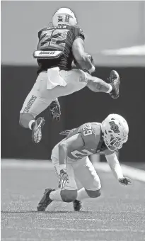  ?? SARAH PHIPPS/THE OKLAHOMAN ?? Oklahoma State’s Jaylen Warren (22) jumps over Cole Stanley (29) during the Cowboys’ spring game at Boone Pickens Stadium in April.