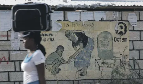  ??  ?? A woman walks past an Oxfam sign in Corail, a camp for displaced people of the 2010 earthquake, in Port-au-Prince