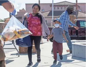  ??  ?? A person hands a bag filled with pasta, rice and other essentials to a mother and her son at a food distributi­on event in Salinas,calif., last month. Food banks are worried about keeping those in need fed amid the coronaviru­s pandemic.