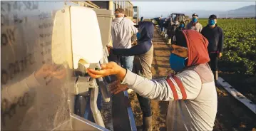  ?? Getty Images/tns ?? In this file photo, farm laborers with Fresh Harvest wash their hands before work on April 28 in Greenfield. They practice social distancing, and receive masks, gloves, hair nets and aprons.