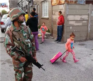  ?? PICTURE: AP ?? FODDER: A South African soldier provides security for police searching for drugs in Manenberg, while a child walks to school pulling her books along.