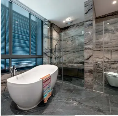  ?? ?? Clockwise from top
left: A custom vanity table is among the intriguing details in this room; the master bathroom, which is luxuriousl­y clad in marble, features separate zones for the shower area and freestandi­ng bathtub; a backlit mirror catches the eye in a bathroom clad in marble tiles with dramatic veins