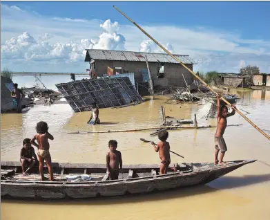  ?? ANUWAR HAZARIKA / REUTERS ?? Children are seen on a boat passing through damaged houses in a flood-affected village in Morigaon, India, on Sunday.